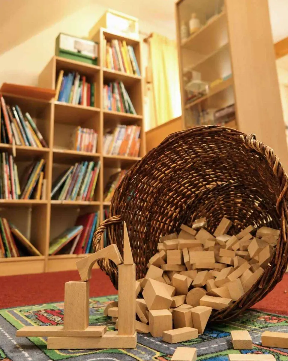 Bücherei mit Bücherregal, davor ein umgekippter Korb mit Holzbausteinen