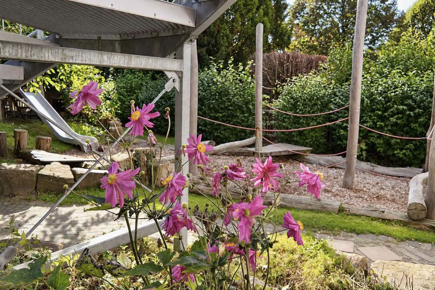 Garten mit blühenden Dahlien, im Hintergrund eine Rutsche und Balancierseile