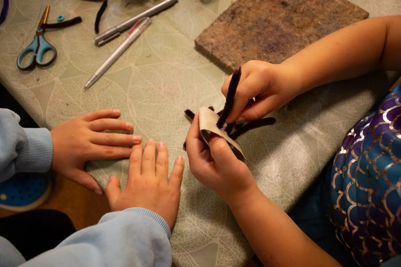 Kinderhände basteln mit einer Schere am Tisch