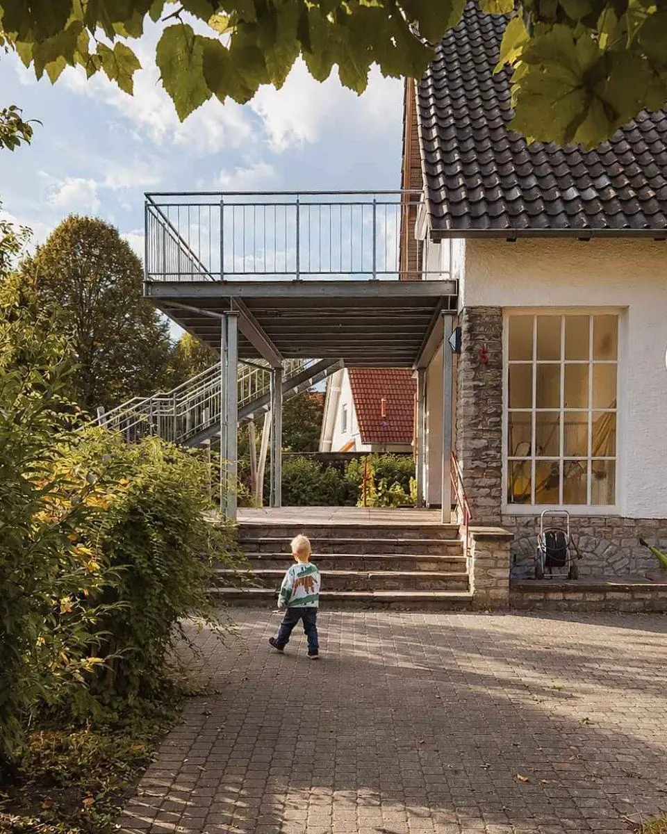 Ein Kind steht auf dem Pflaster vor dem Haupthaus der Villa mit Balkon und Außentreppe