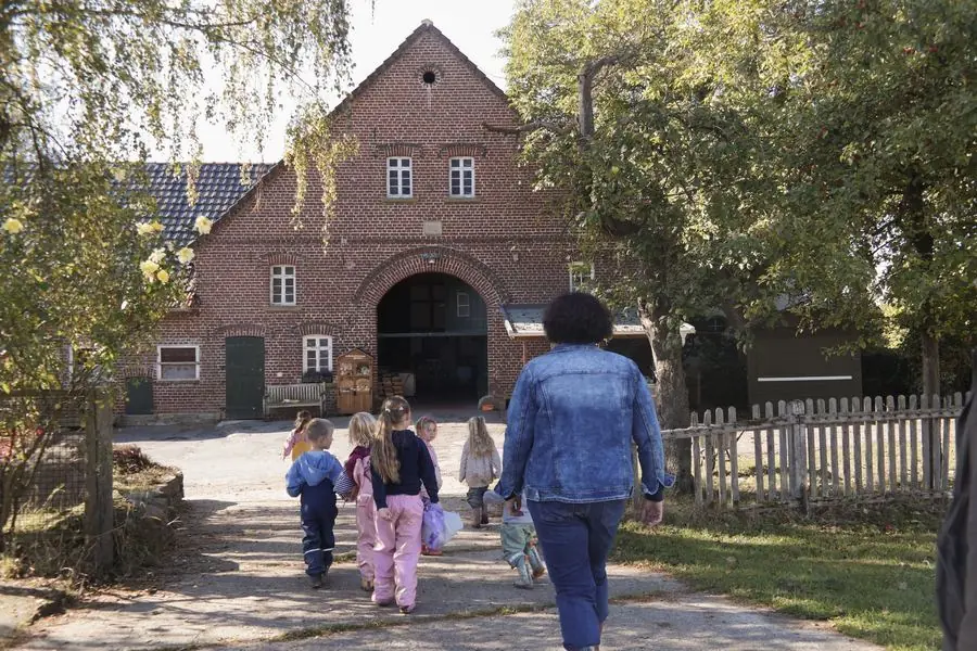 Kinder und eine Erzieherin gehen auf das Backsteinhaus des Hofs Blaurock zu