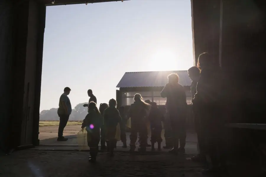 Im Gegenlicht stehen Kinder und Erwachsene im Scheunentor, draußen scheint die Sonne