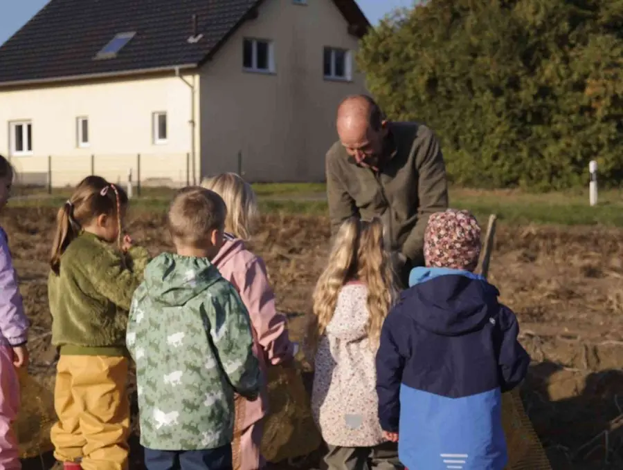 Die Kinder hören dem Landwirt auf dem Acker zu