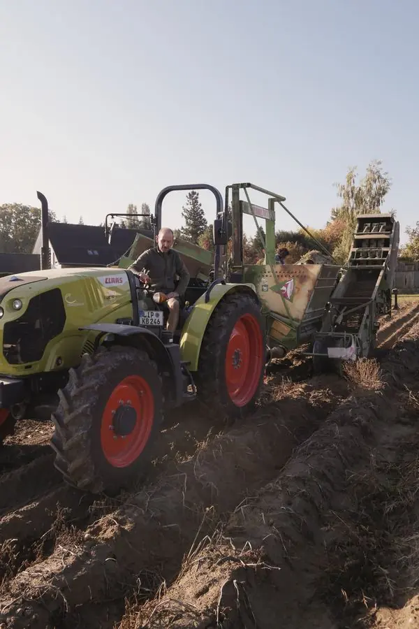 Der Landwirt sitzt auf dem Traktor, an dem der Kartoffelroder hängt