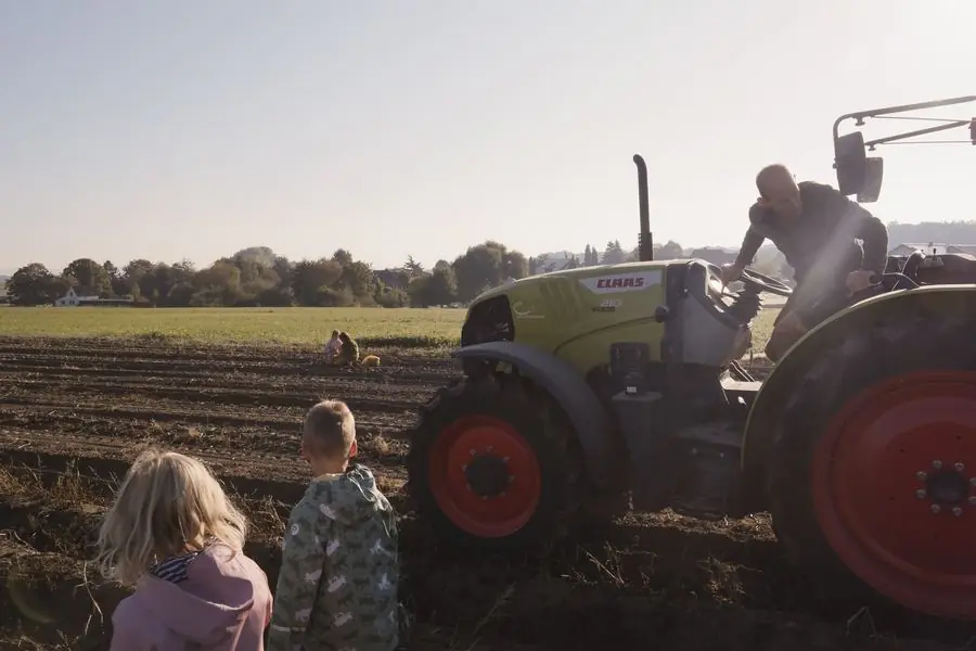 Zwei Kinder stehen am Rand des Ackers und schauen zum Traktor