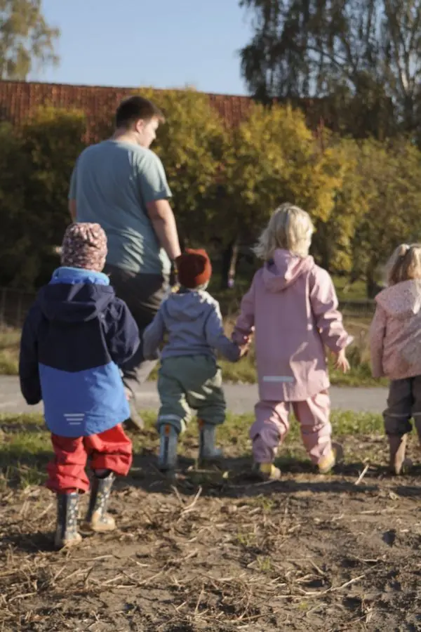 Kinder gehen Hand in Hand mit einem Erwachsenen über den Acker, alle von hinten