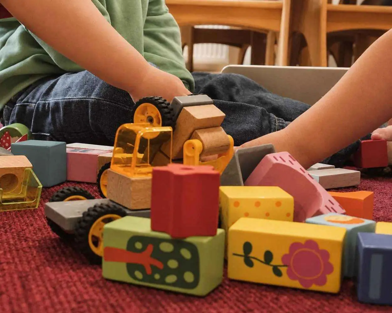 Holzbagger und bunte Bausteine auf einem roten Teppich, Kinderhände spielen damit