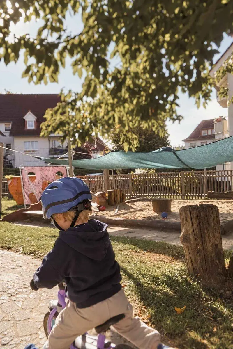 Ein Kind in blauem Helm fährt mit dem Laufrad durch den Garten