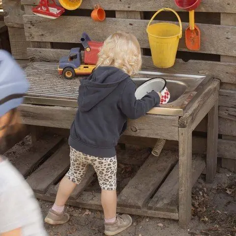 Ein Kind probiert an der Matschküche aus Holzpaletten mit Wasser und Eimern