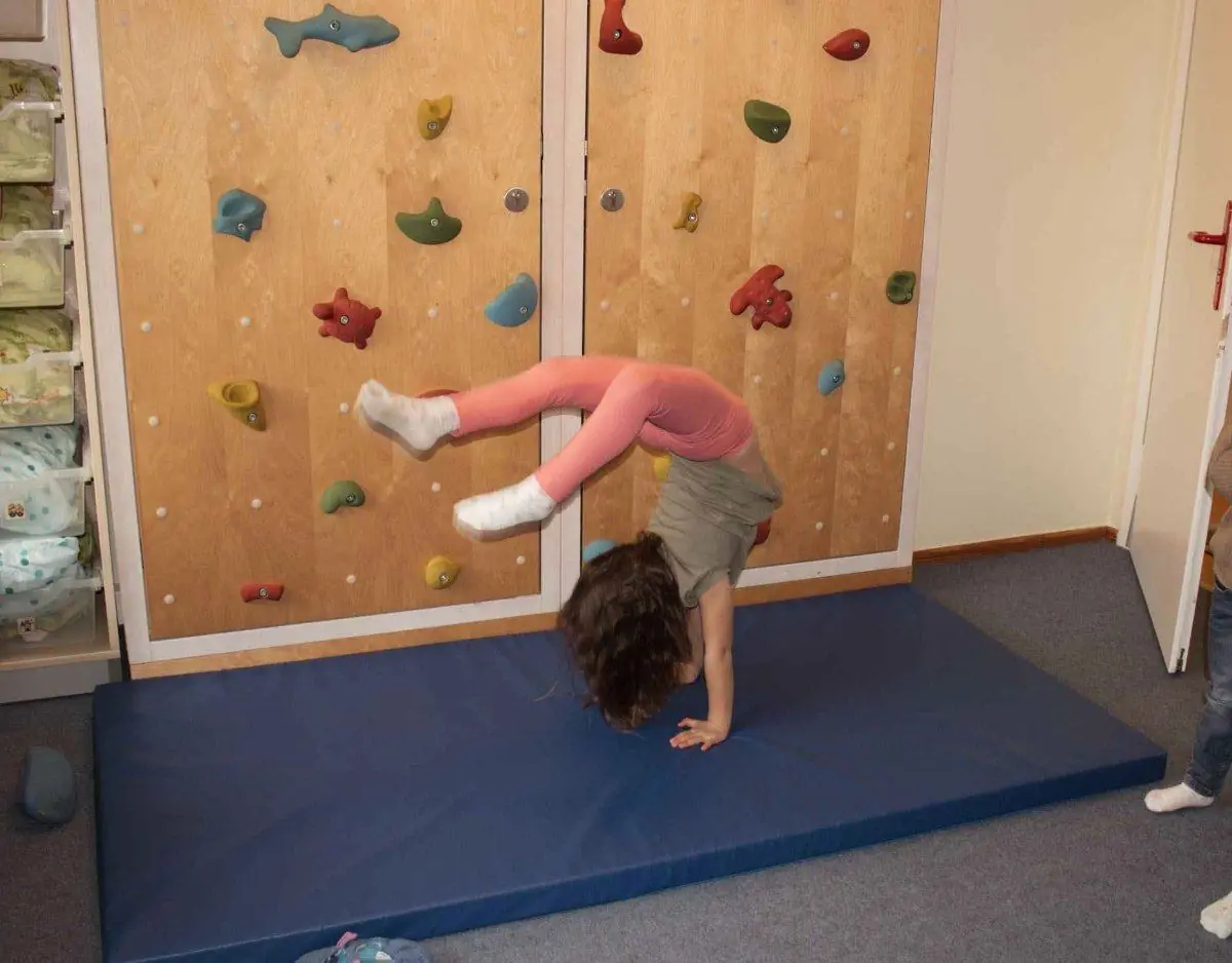 Ein Kind macht an der Kletterwand einen Handstand auf einer blauen Matte