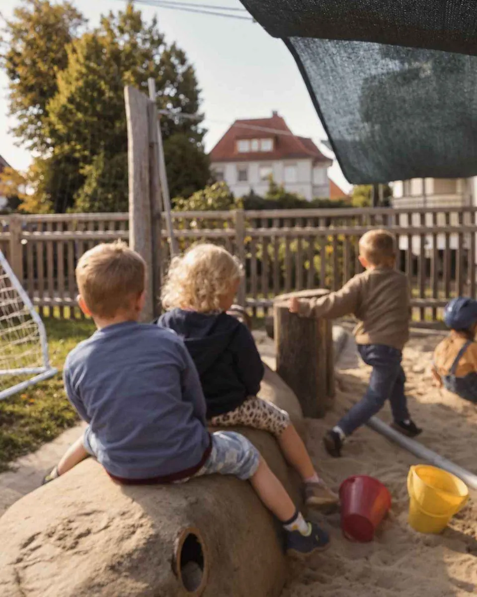 Mehrere Kinder sitzen und spielen auf einem Sandstein im Sandbereich