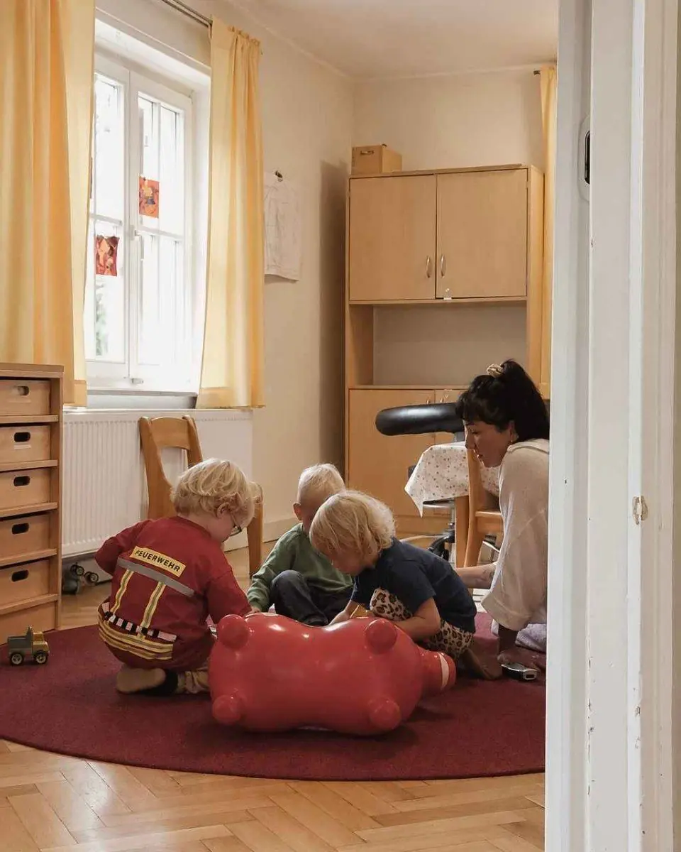 Kinder und eine Erzieherin im Raum der Kleinsten mit rotem Teppich und Hüpftier