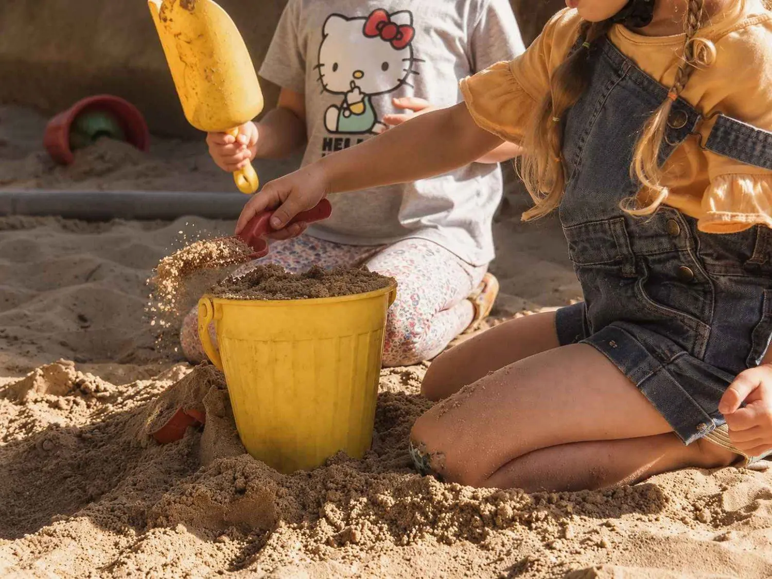 Kinder spielen mit einem gelben Eimer im Sandkasten