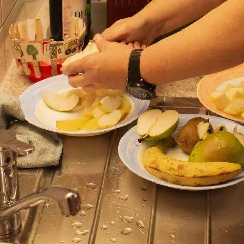 Teller mit Apfel, Birne und Banane, eine Hand schneidet Obst in der Küche