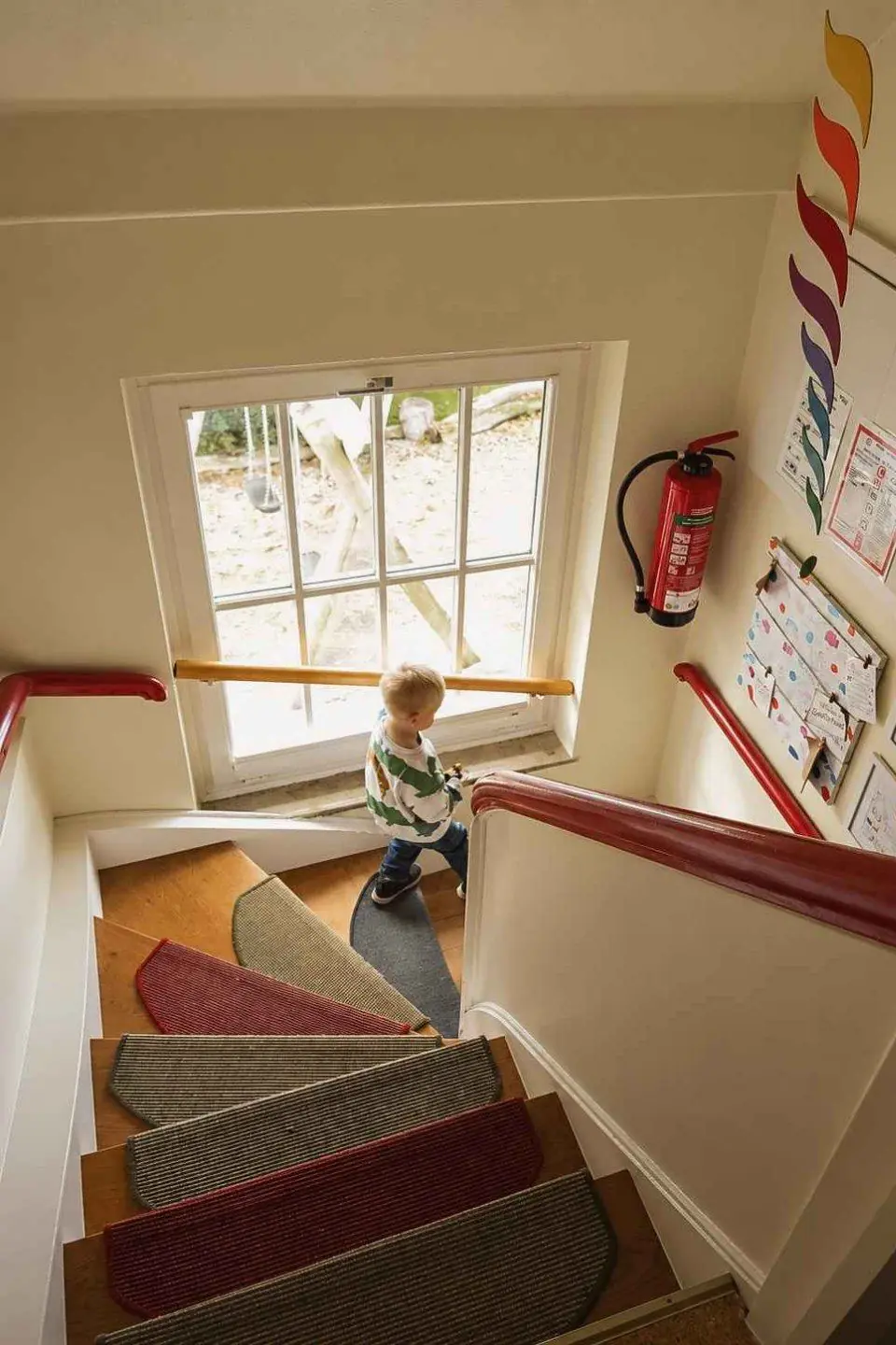 Blick in das Treppenhaus mit Fenster, ein Kind steigt die Treppe hinauf